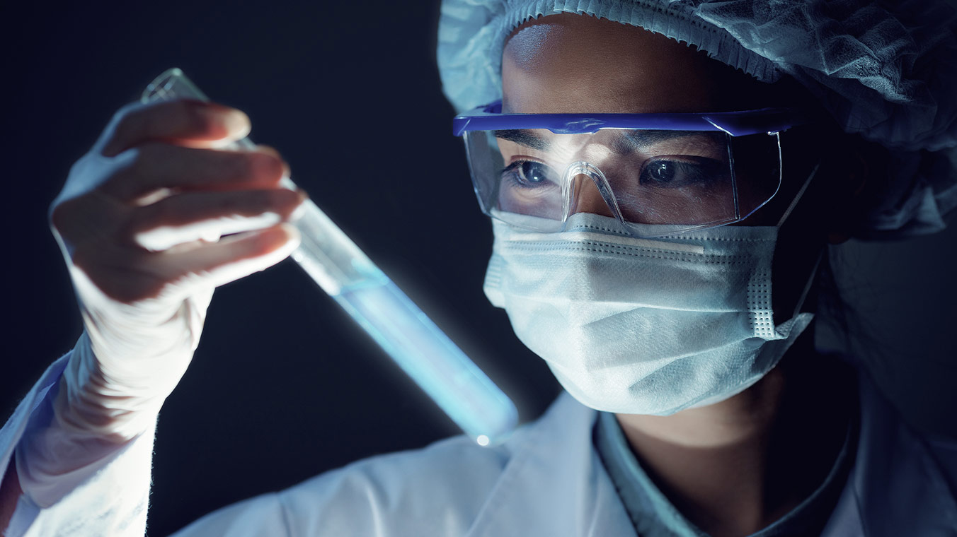 Woman in a mask and safety goggles inspecting a test tube