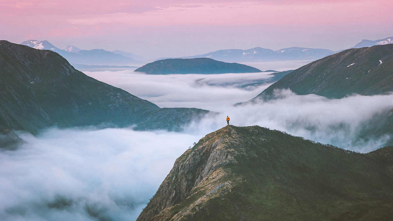 Person standing on a mountain with mist surrounding