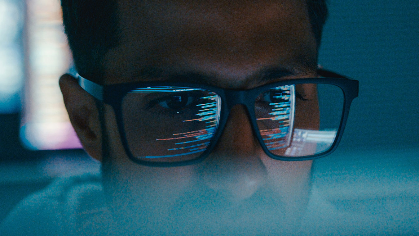 MAn in glasses with computer code reflecting off of them